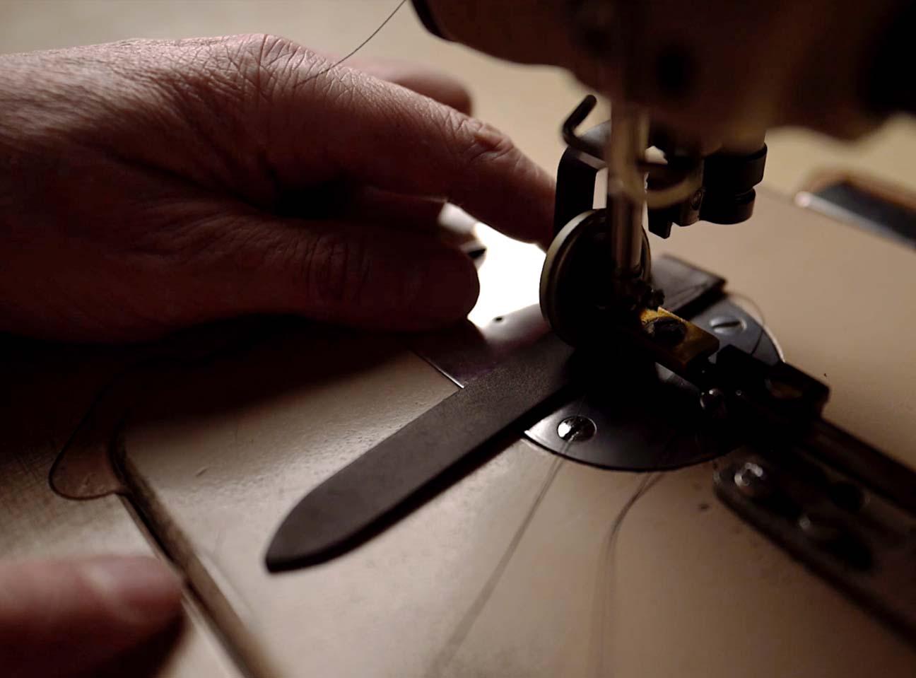 Hand guiding leather watch strap under sewing machine.
