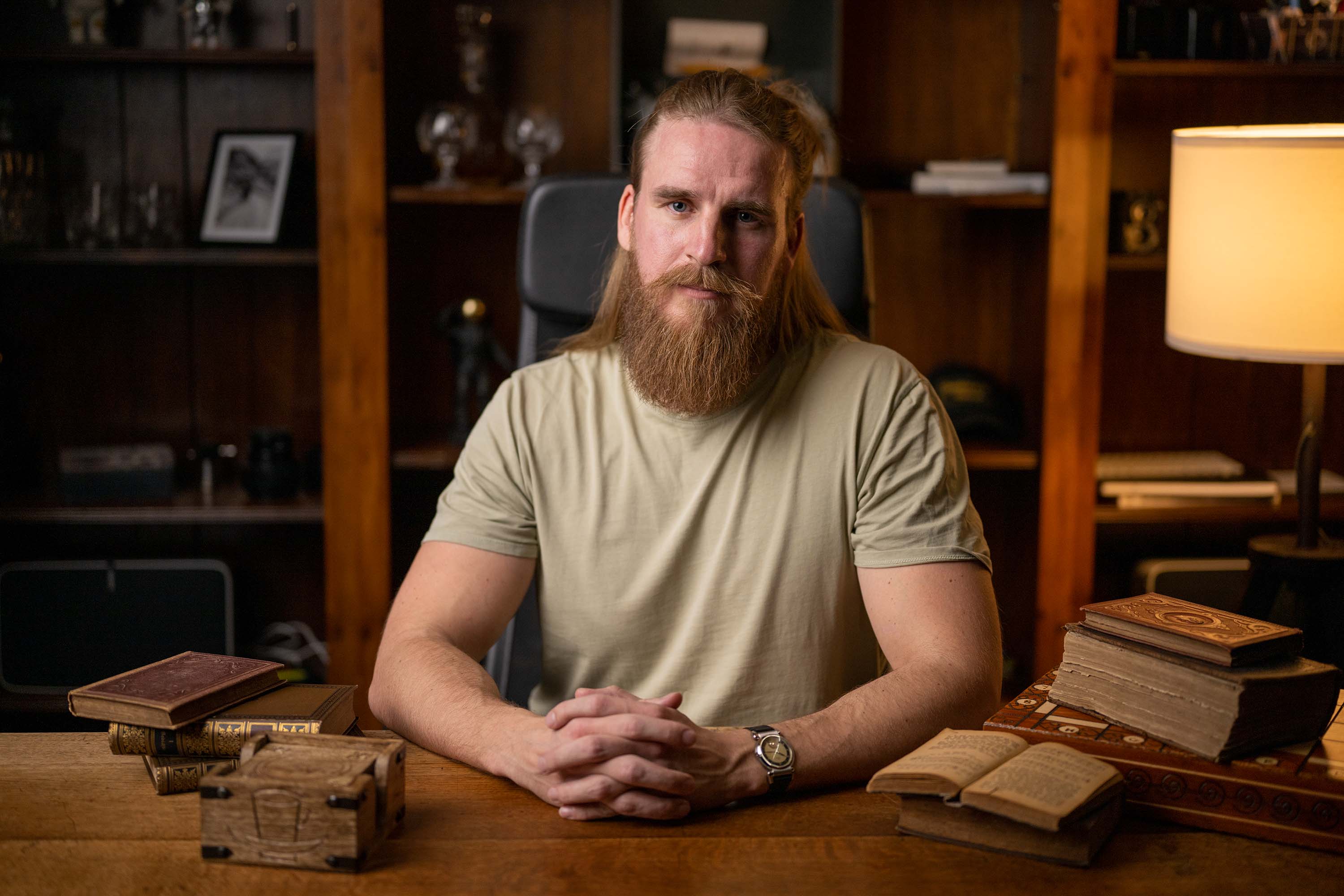 Hombre de barba larga con camiseta beige, sentado a una mesa.